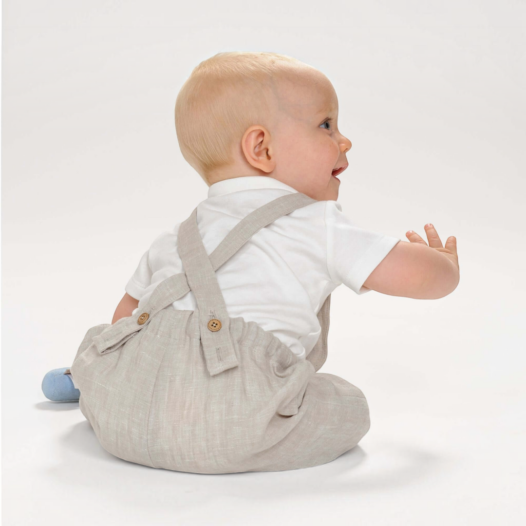 Patternforkids Kleinkind Latzhose MAX aus beigem Leinenstoff mit Knöpfen, getragen von einem Baby in Seitenansicht