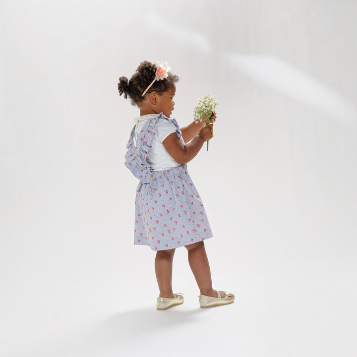 Latzkleid PDF Schnittmuster LIVIA – Rüschenkleid mit Trägern 68/74–116/122, Mädchen in floralem Kleid hält Blumen.