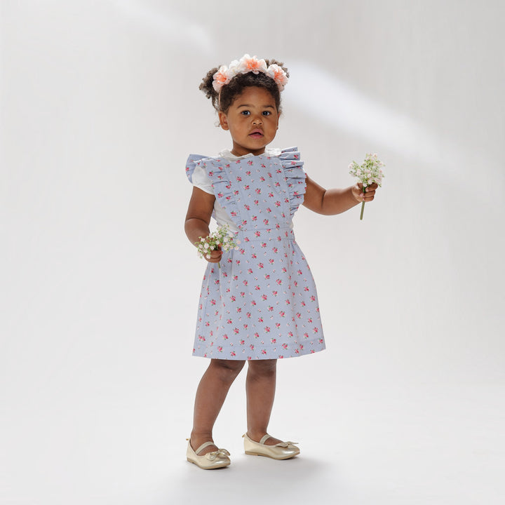 Latzkleid PDF Schnittmuster LIVIA – Rüschenkleid mit Trägern 68/74–116/122, kleines Mädchen hält Blumen und trägt Kleid mit Rüschen.