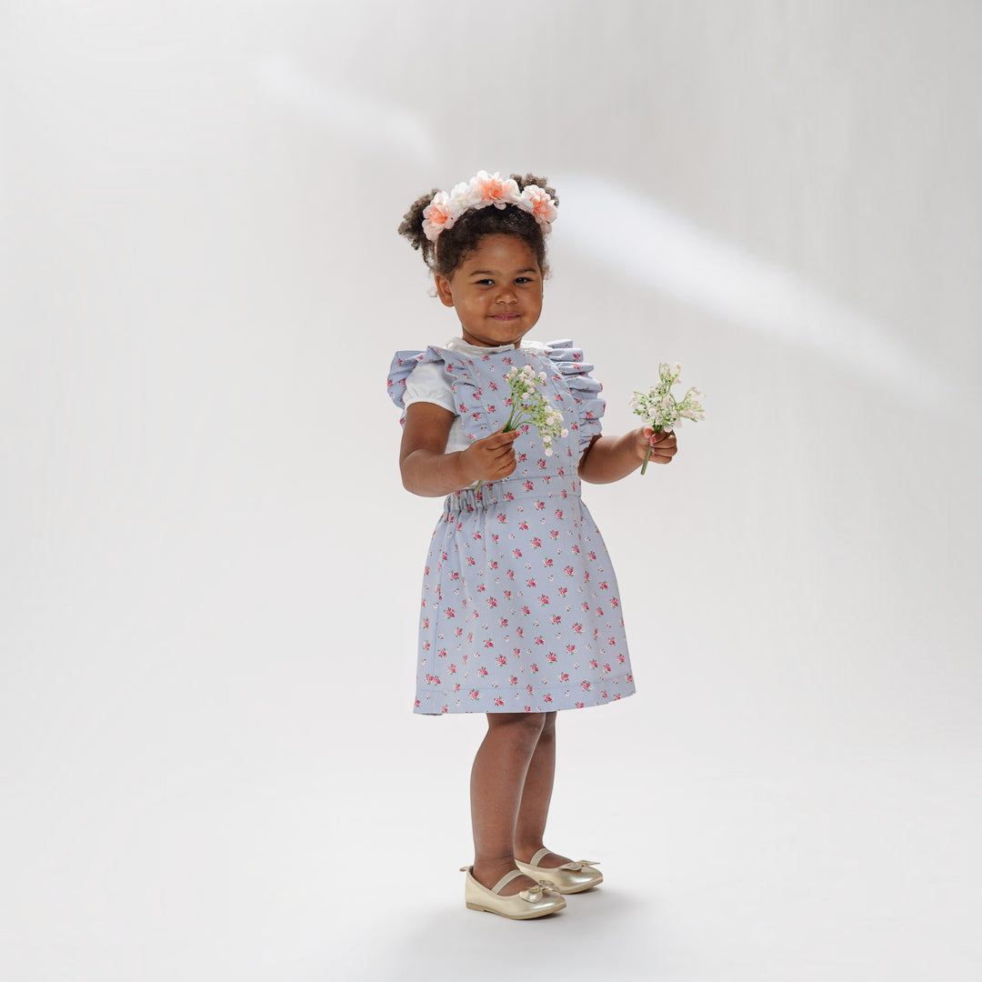 Latzkleid PDF Schnittmuster LIVIA – Rüschenkleid mit Trägern 68/74–116/122, Mädchen in floralem Kleid hält Blumen.
