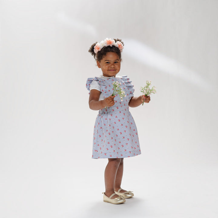 Latzkleid PDF Schnittmuster LIVIA – Rüschenkleid mit Trägern 68/74–116/122, Mädchen in floralem Kleid hält Blumen.