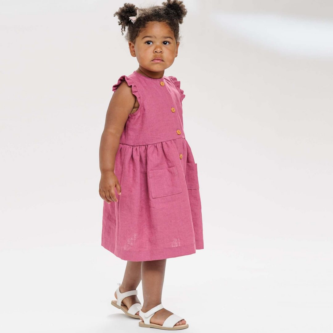 Kleines Mädchen trägt ein altrosa ärmelloses Patternforkids Kleid mit Rüschen und aufgesetzten Taschen