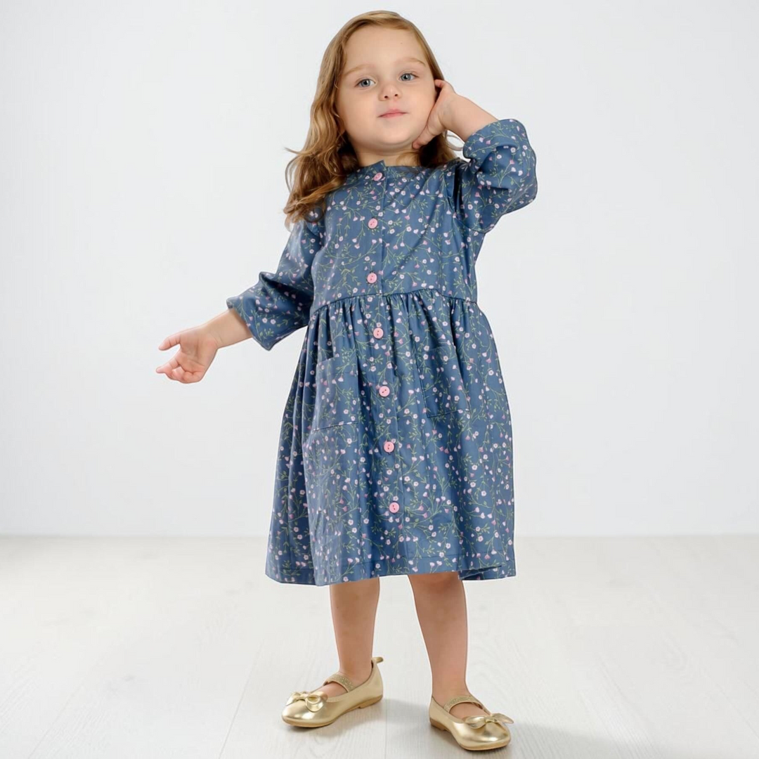 Patternforkids Mädchenkleid MIMI aus blauem Stoff mit Blumenmuster, Knopfleiste und langen Ärmeln an einem kleinen Mädchen