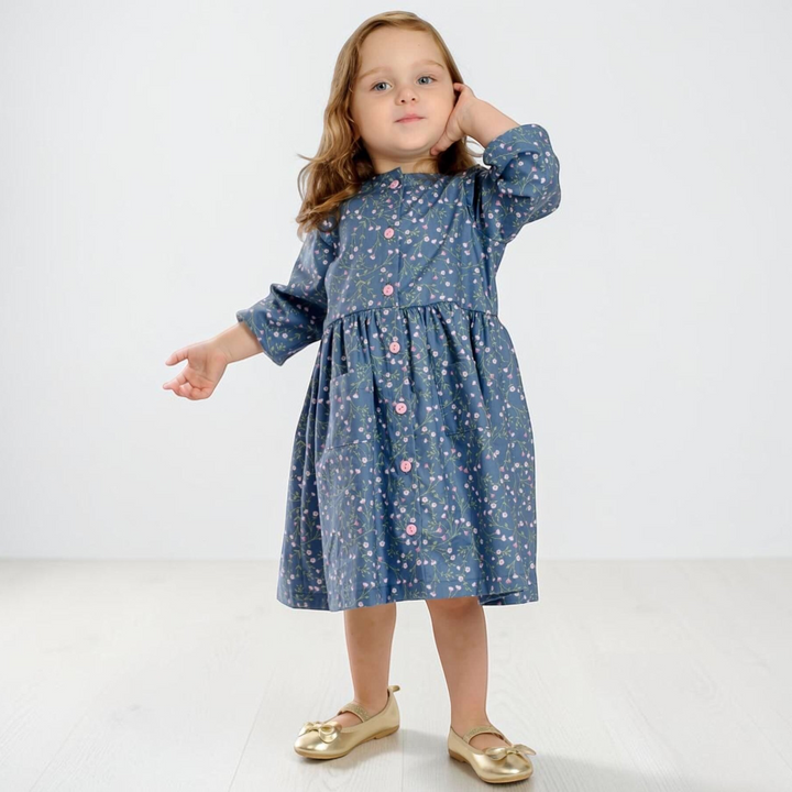 Patternforkids Mädchenkleid MIMI aus blauem Stoff mit Blumenmuster, Knopfleiste und langen Ärmeln an einem kleinen Mädchen