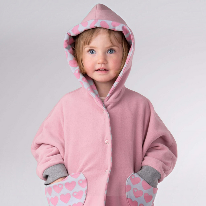 Patternforkids Schnittmuster Poncho MARA in Rosa mit Kapuze, Herz-Muster-Details und Druckknöpfen an einem Kind