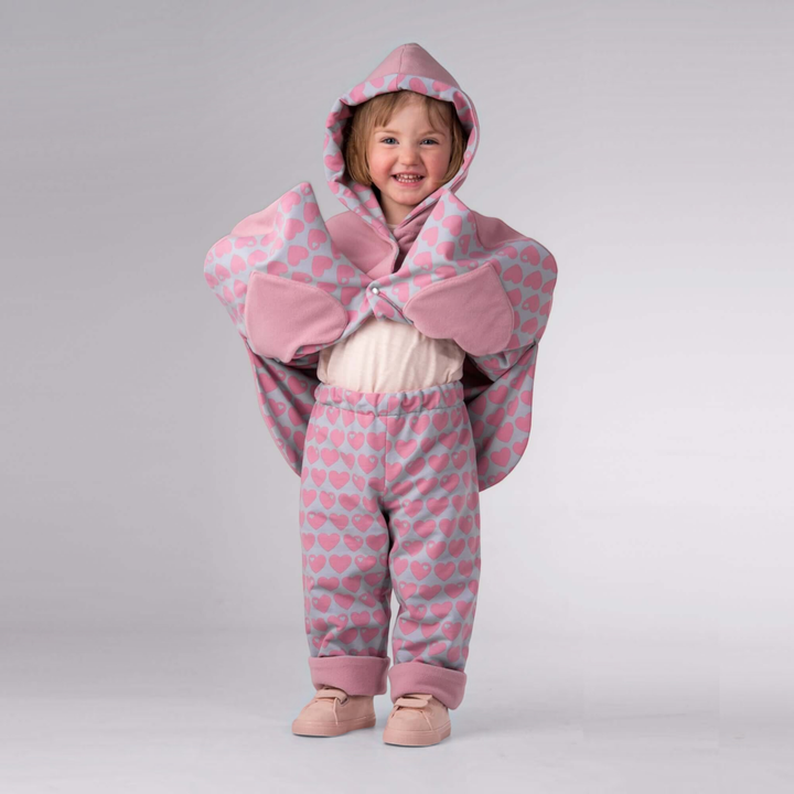 Kind trägt Patternforkids Poncho MARA und Wendehose FIOCCO mit rosa Herzmuster, Kapuze und bequemen Bündchen