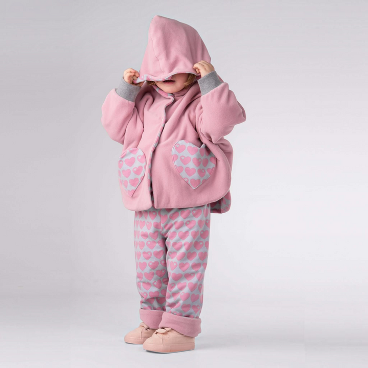 Kind trägt Patternforkids Poncho MARA und Wendehose FIOCCO in Rosa mit Herzmuster aus weichem Fleece