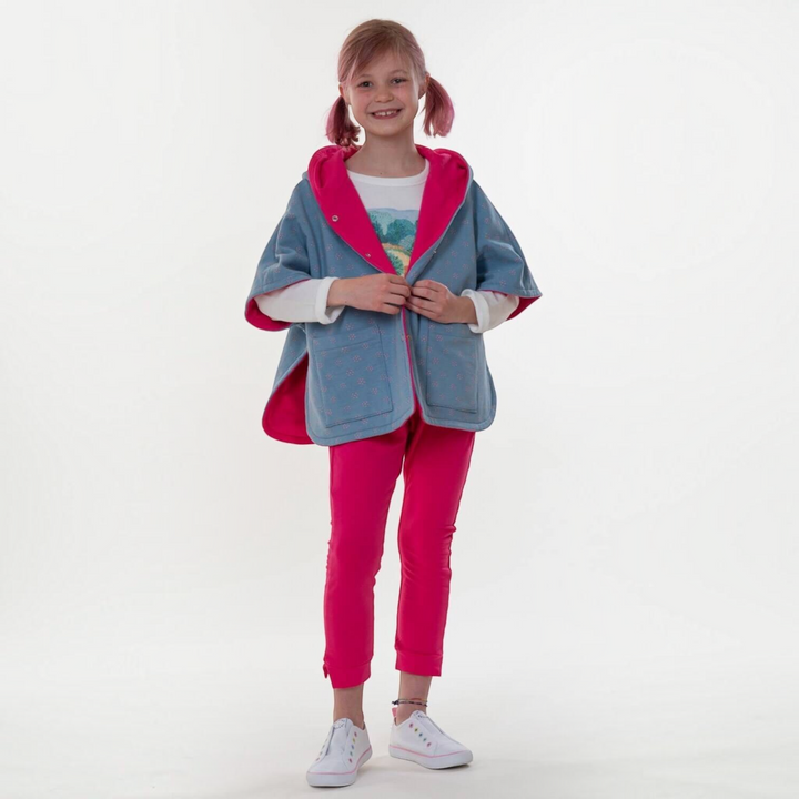 Patternforkids Schnittmuster Mädchen Poncho Paula mit Kapuze in Blau und Pink, getragen von einem jungen Mädchen