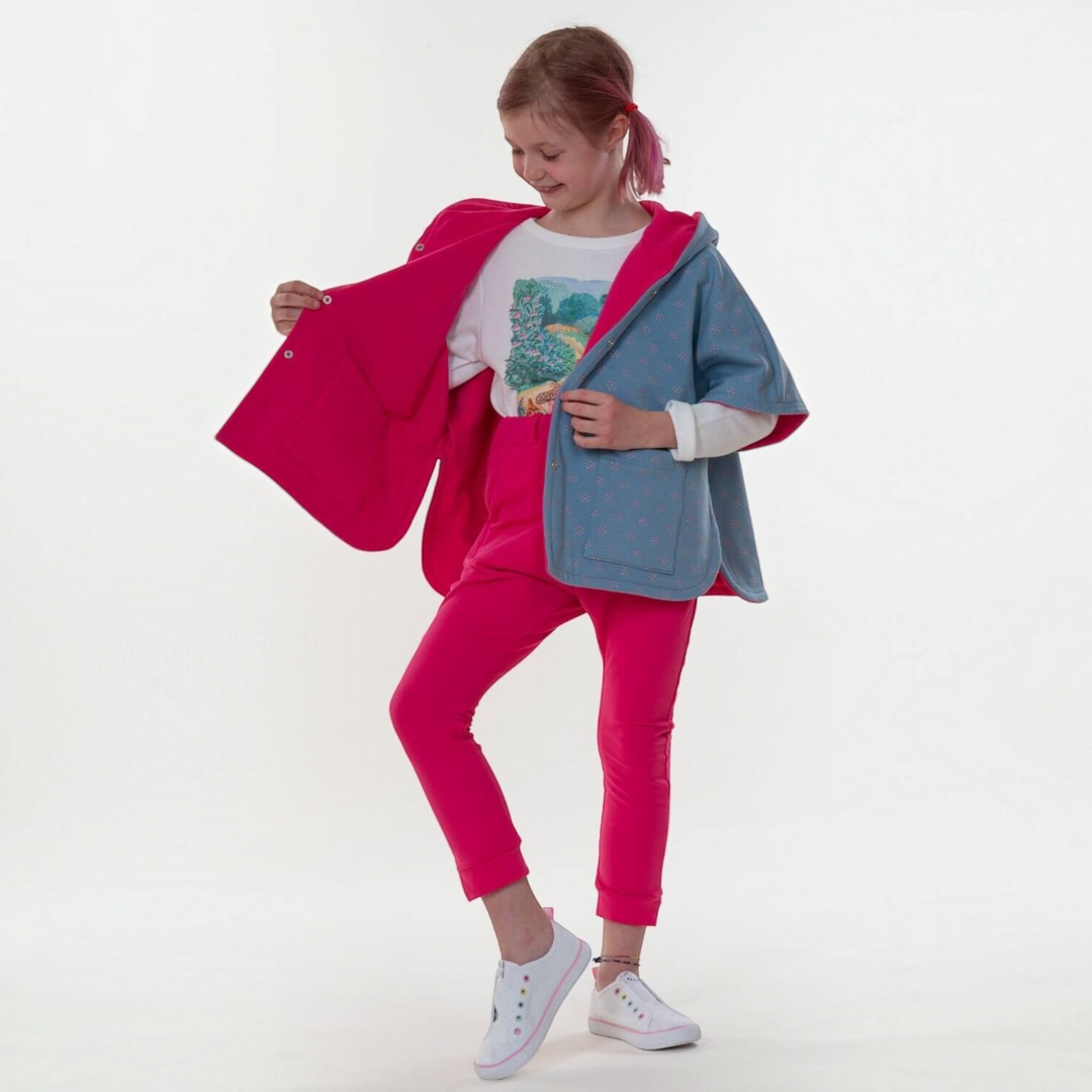 Patternforkids Schnittmuster Mädchen Poncho PAULA mit Kapuze in Blau und Pink, getragen von einem Mädchen.