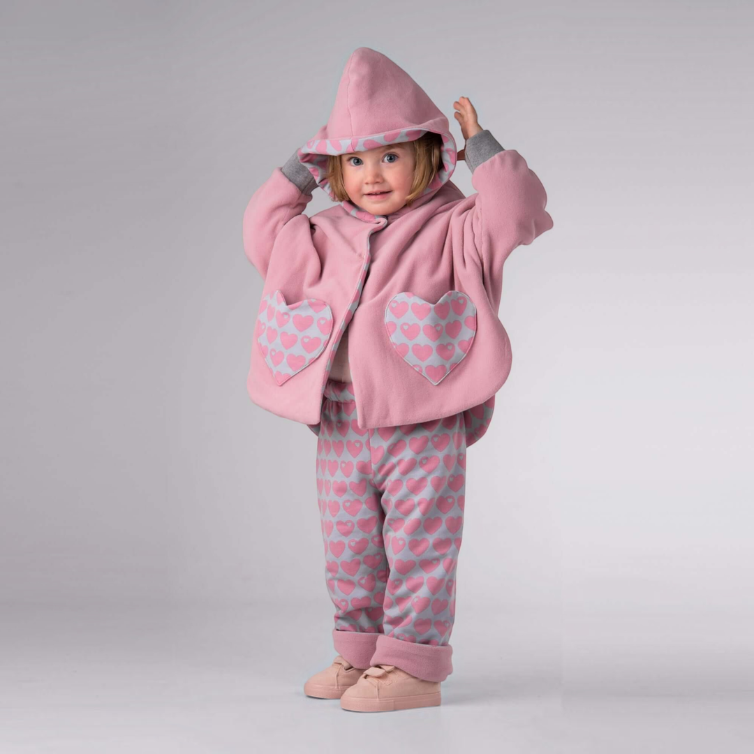 Patternforkids Schnittmuster Set MARA FIOCCO: Kind trägt rosa Poncho mit Herz-Taschen und passende Wendehose mit Herzmuster