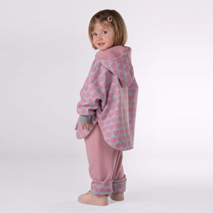 Patternforkids Wendeponcho MARA mit Kapuze aus rosa Fleece mit Herzmuster, getragen von einem kleinen Mädchen.