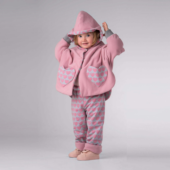 Patternforkids Wendeponcho MARA aus rosa Fleece mit Kapuze und herzförmigen Taschen an einem Kleinkind