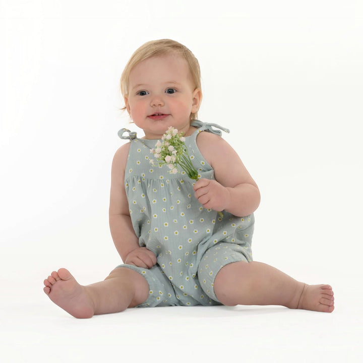 Schnittmuster Baby Mädchen Jumpsuit NELE PDF - Baby im blauen Jumpsuit mit Blumen hält Blumenstrauß.