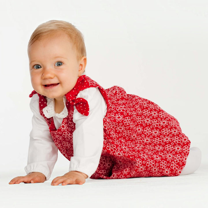 Baby Set PDF Schnittmuster BABY TWINSET – Trägerkleider & Pumphose 50/56–98/104: Kleines Mädchen in rotem Kleid, lächelnd und auf den Knien.
