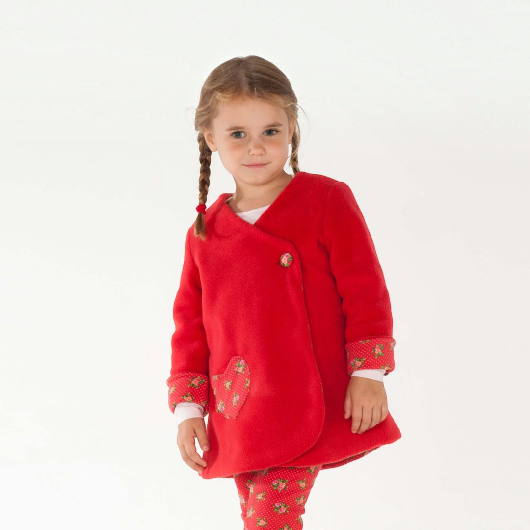 Mädchen trägt ein rotes ärmelloses Wickelkleid aus Fleece mit herzförmiger Tasche, Teil des Wickelkleid Schnittmuster MARIE PDF – 3 Varianten 92/98–128/134.