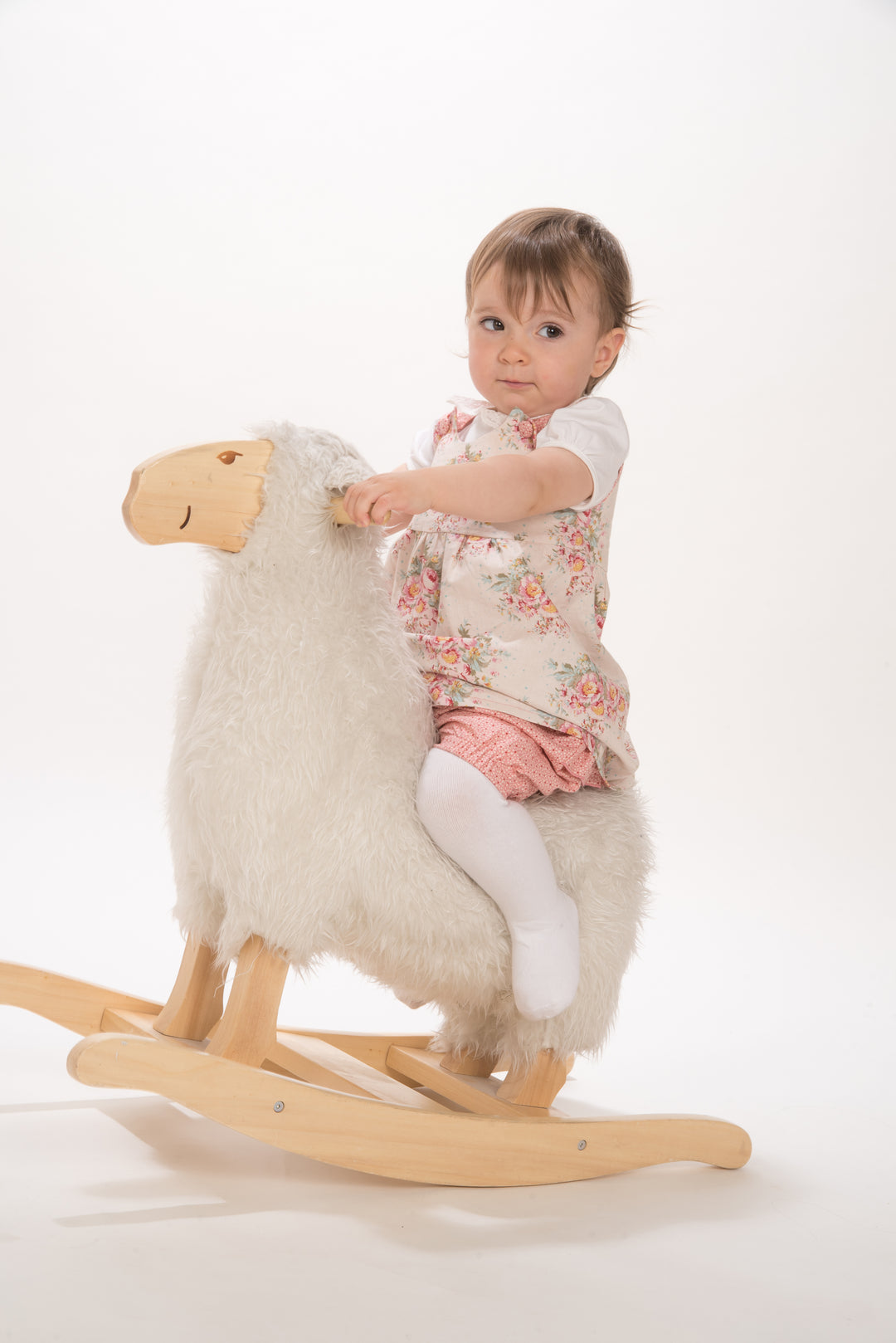 Schnittmuster Baby Twinset Babykleid Hängerchen und Pumphose, Baby auf einem Holz-Schaukel-Schaf mit einem blumigen Kleid.