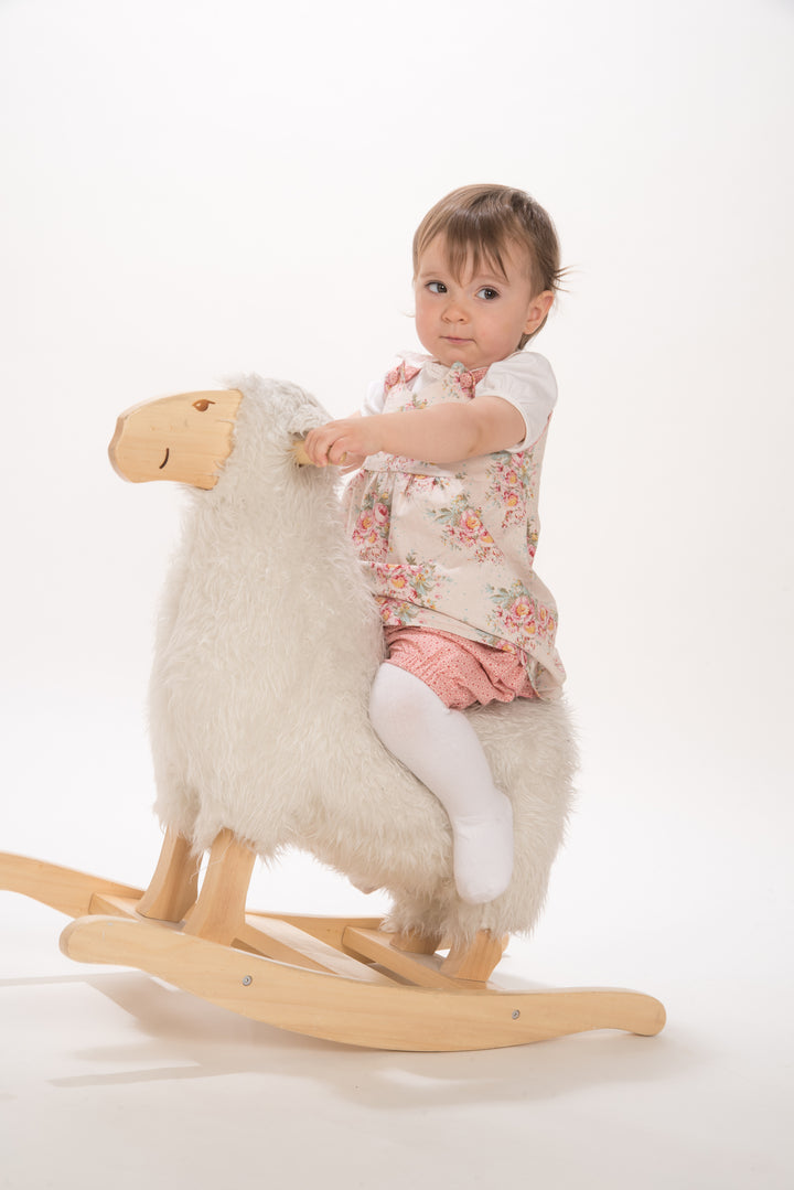 Schnittmuster Baby Twinset Babykleid Hängerchen und Pumphose, Baby auf einem Holz-Schaukel-Schaf mit einem blumigen Kleid.